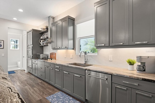 kitchen with light stone counters, stainless steel appliances, sink, gray cabinets, and dark hardwood / wood-style floors