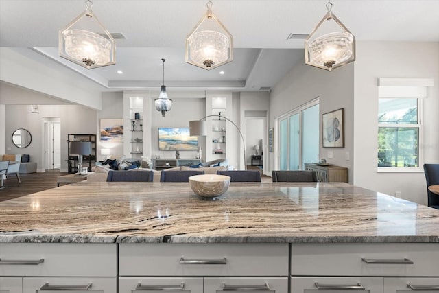 kitchen featuring a tray ceiling, light stone counters, white cabinets, and decorative light fixtures