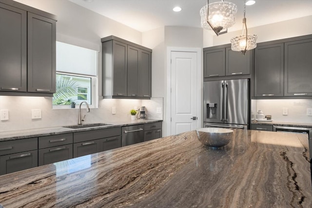 kitchen featuring light stone counters, stainless steel appliances, sink, pendant lighting, and gray cabinets