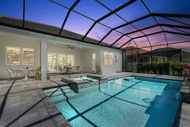 pool at dusk featuring an in ground hot tub, a patio area, ceiling fan, and a lanai