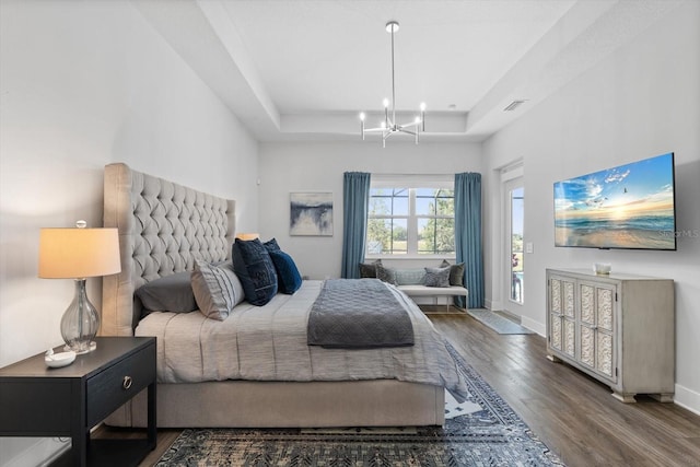 bedroom with access to exterior, a raised ceiling, dark hardwood / wood-style floors, and an inviting chandelier