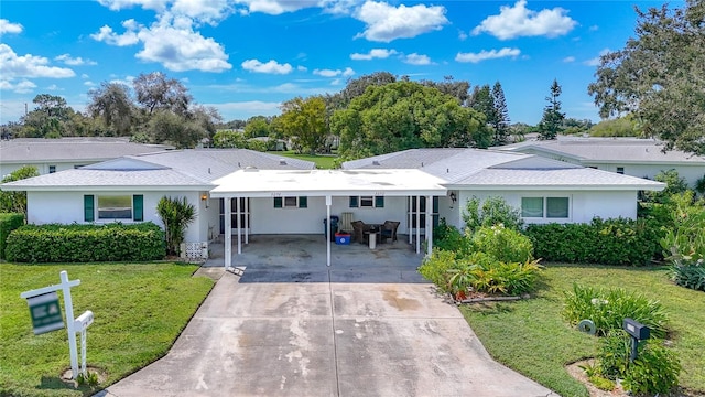 back of property with stucco siding, a carport, a yard, and concrete driveway