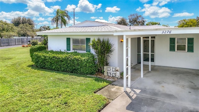 view of front of house featuring stucco siding, fence, roof with shingles, and a front yard