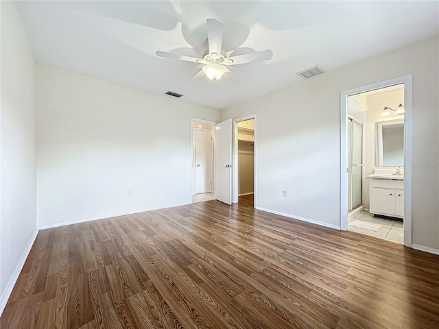 unfurnished bedroom featuring a walk in closet, connected bathroom, light wood-type flooring, and ceiling fan