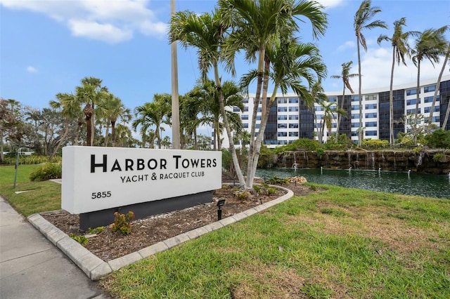 community / neighborhood sign featuring a water view and a lawn