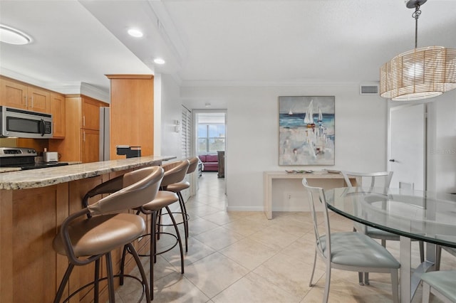 kitchen featuring light stone counters, stainless steel appliances, visible vents, a kitchen bar, and crown molding