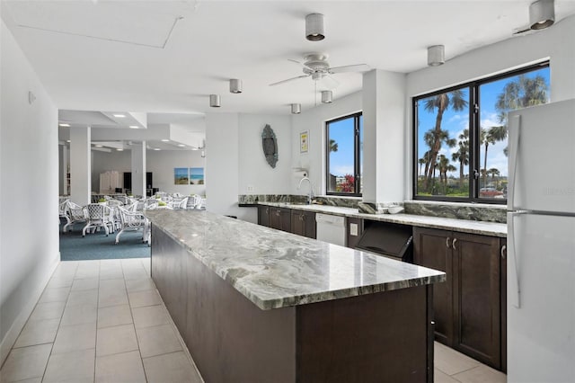 kitchen with ceiling fan, light stone counters, light tile patterned flooring, dark brown cabinetry, and white appliances