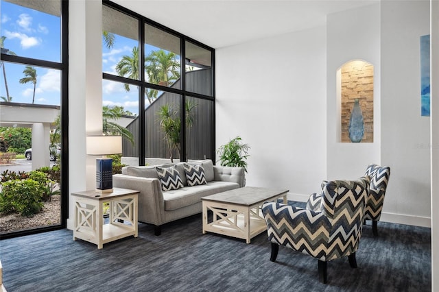 living area featuring a towering ceiling, baseboards, and a wall of windows