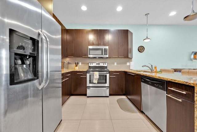 kitchen with hanging light fixtures, light stone counters, light tile patterned floors, stainless steel appliances, and sink