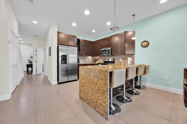 kitchen featuring appliances with stainless steel finishes, decorative light fixtures, a kitchen bar, dark brown cabinetry, and kitchen peninsula