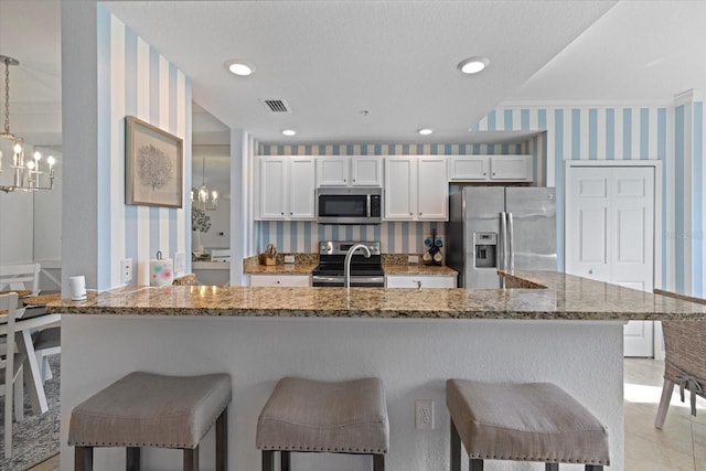 kitchen with a kitchen breakfast bar, white cabinets, pendant lighting, and appliances with stainless steel finishes