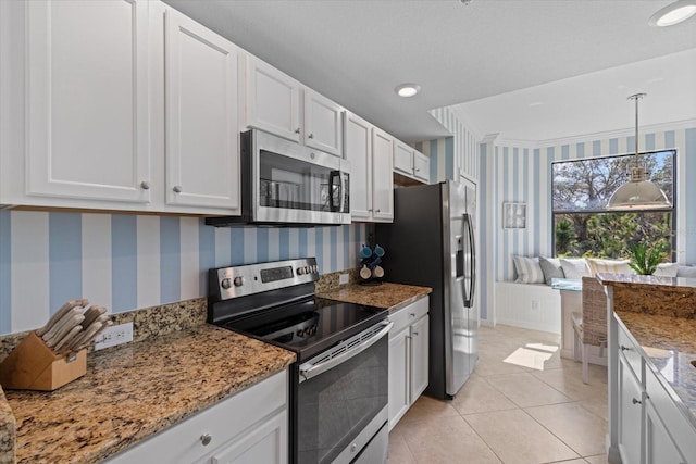 kitchen with white cabinets, decorative light fixtures, light tile patterned floors, stone countertops, and stainless steel appliances