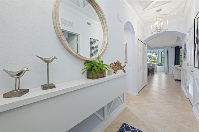 corridor with ornamental molding, a towering ceiling, light tile patterned flooring, and an inviting chandelier