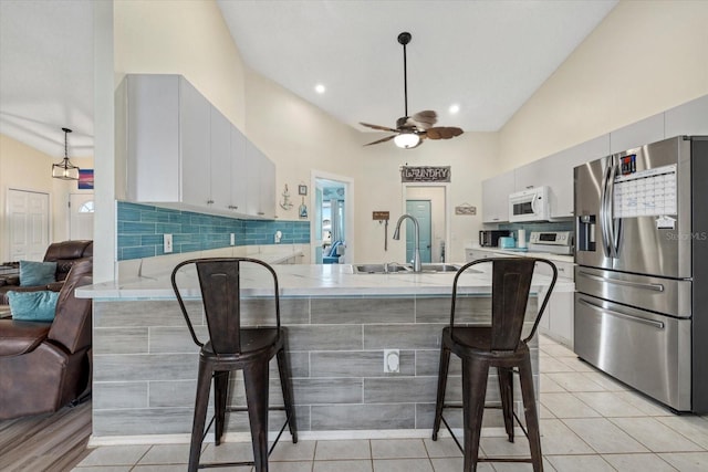 kitchen featuring a breakfast bar area, kitchen peninsula, stainless steel fridge with ice dispenser, light tile patterned flooring, and white cabinetry