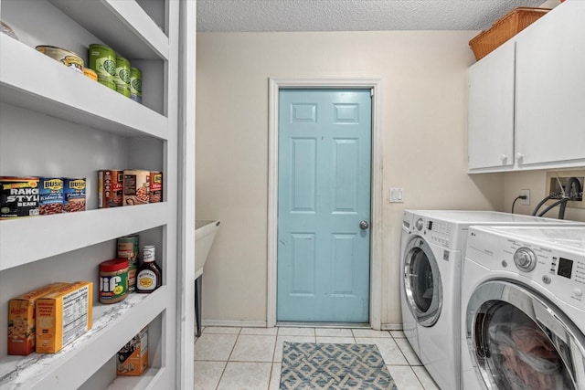 washroom with a textured ceiling, light tile patterned flooring, washing machine and dryer, and cabinet space