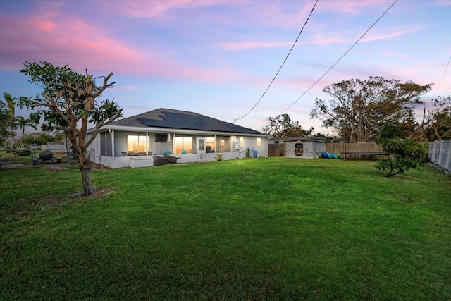 back house at dusk with a yard and a sunroom