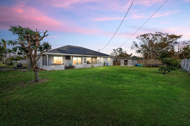 rear view of house featuring roof mounted solar panels, a fenced backyard, and a yard