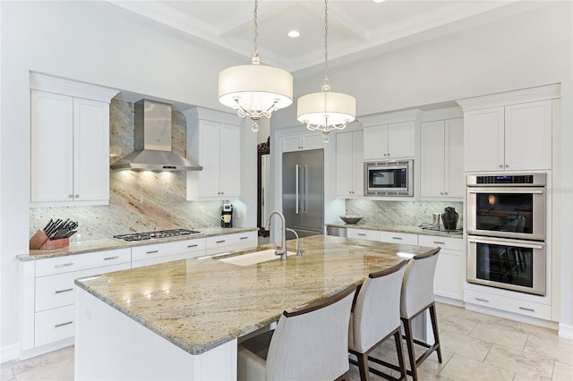 kitchen featuring built in appliances, wall chimney exhaust hood, sink, and an island with sink