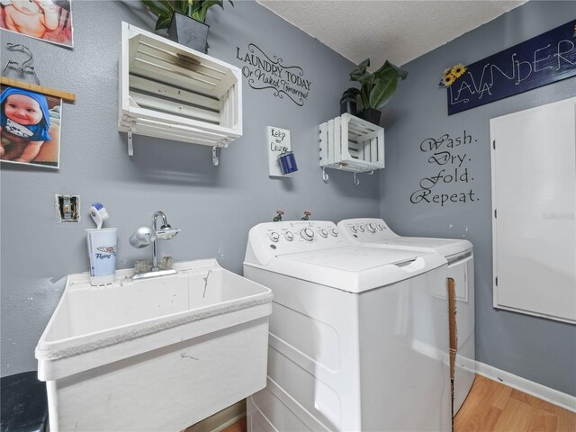 clothes washing area featuring a textured ceiling, light wood-type flooring, sink, and washing machine and dryer