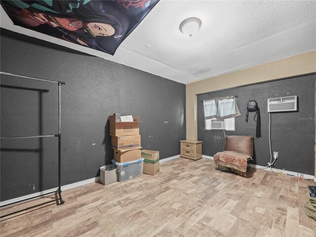 sitting room with light hardwood / wood-style flooring, cooling unit, a wall unit AC, and a textured ceiling