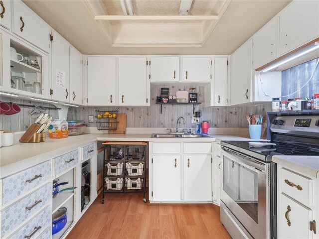 kitchen with a tray ceiling, white cabinetry, sink, and electric range