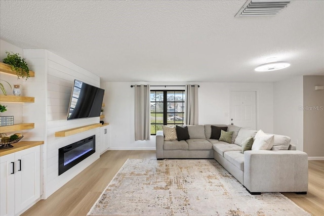 living room with a large fireplace, a textured ceiling, and light wood-type flooring