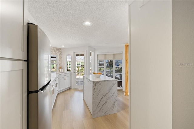 kitchen with stainless steel fridge, light wood-type flooring, white cabinetry, a textured ceiling, and a center island