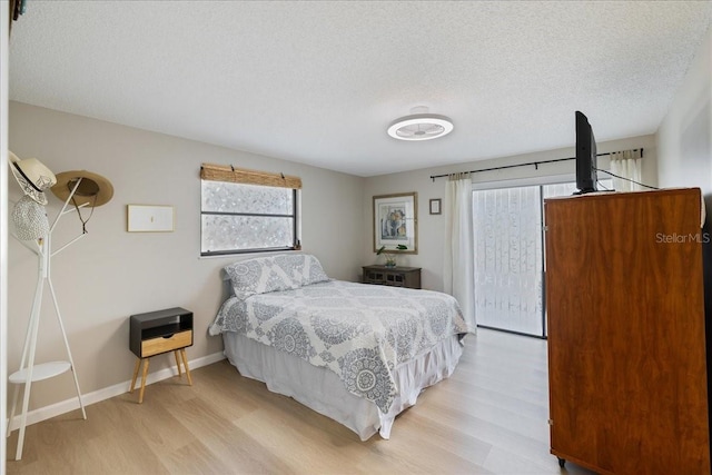 bedroom with a textured ceiling, light hardwood / wood-style floors, and multiple windows