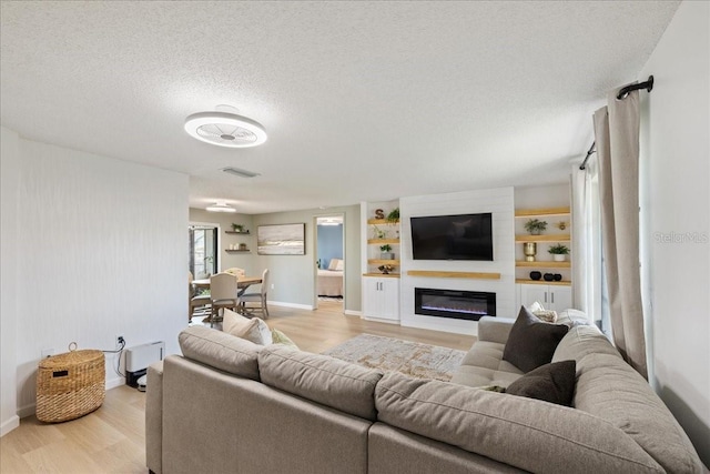 living room with a fireplace, a textured ceiling, and light hardwood / wood-style flooring