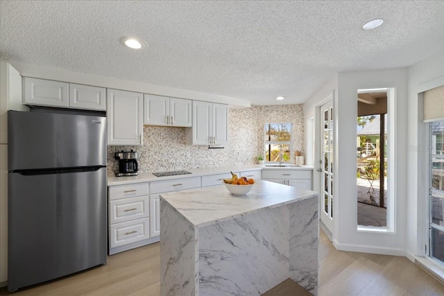 kitchen with white cabinetry, a textured ceiling, stainless steel fridge, and light wood-type flooring