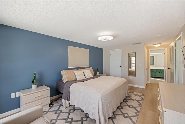 bedroom featuring light wood-type flooring, a textured ceiling, and ensuite bathroom