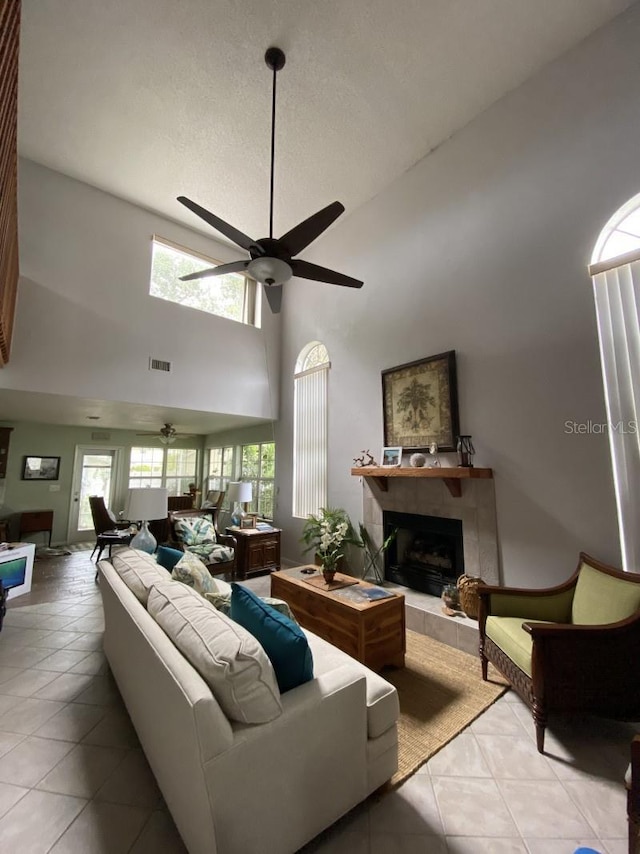 tiled living room with plenty of natural light, ceiling fan, a tile fireplace, and a high ceiling