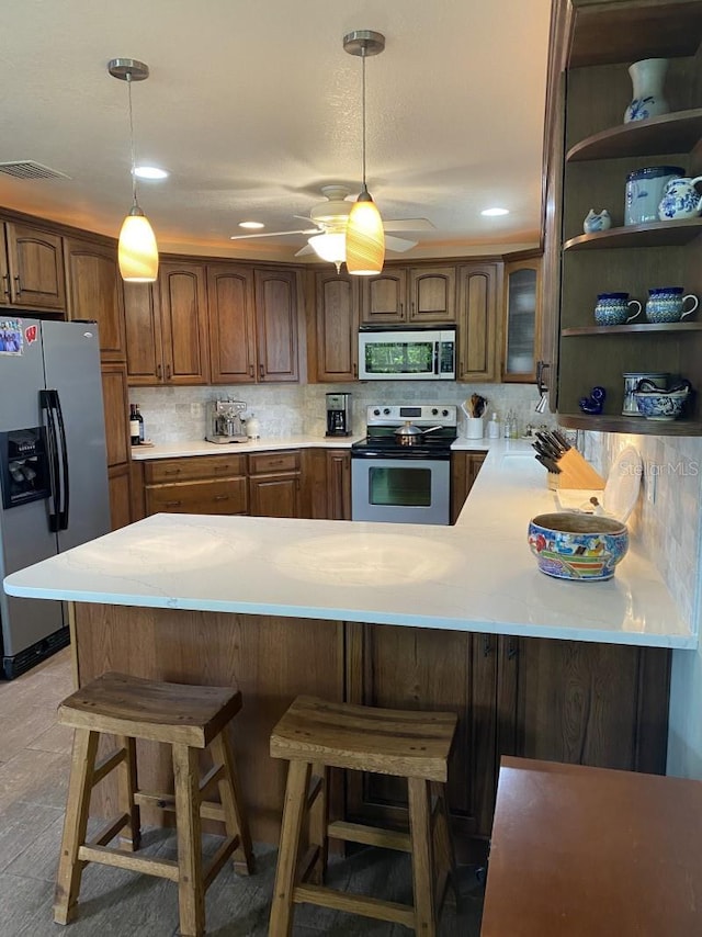 kitchen with ceiling fan, stainless steel appliances, a kitchen breakfast bar, kitchen peninsula, and decorative backsplash