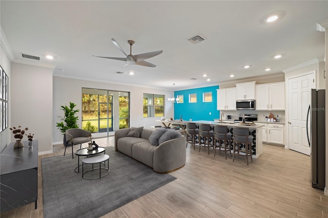 living room featuring ornamental molding, sink, ceiling fan with notable chandelier, and light wood-type flooring