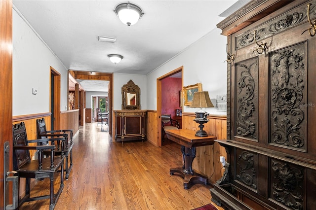 hall with hardwood / wood-style floors, ornamental molding, and wooden walls