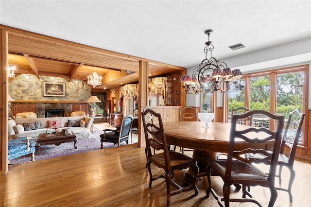 dining room with a stone fireplace, hardwood / wood-style flooring, and a notable chandelier