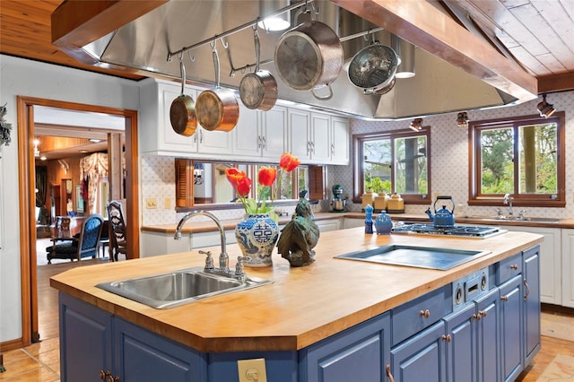 kitchen with sink, wood counters, blue cabinets, a kitchen island with sink, and white cabinets