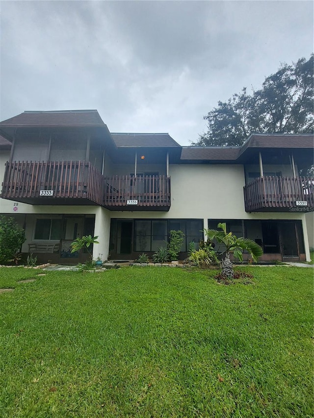 back of property with a balcony and a lawn