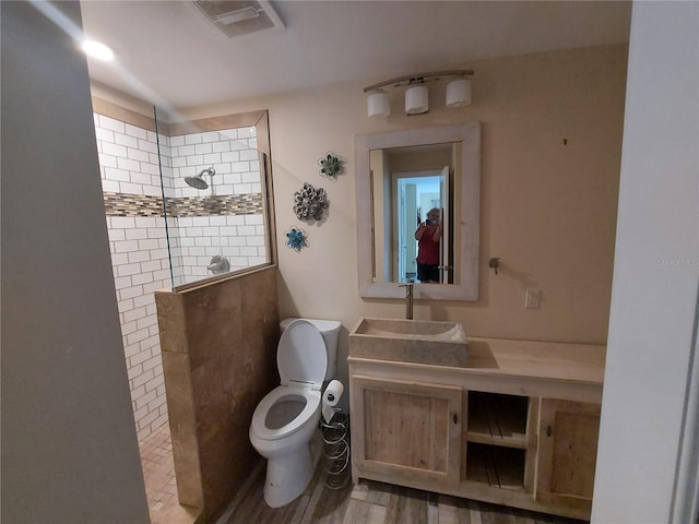 bathroom with hardwood / wood-style flooring, a tile shower, vanity, and toilet