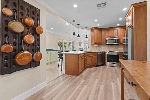 kitchen featuring hanging light fixtures, stainless steel appliances, a kitchen breakfast bar, kitchen peninsula, and ornamental molding