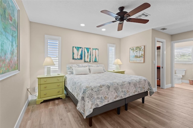 bedroom with ensuite bathroom, light hardwood / wood-style flooring, ceiling fan, and a textured ceiling