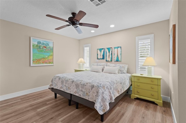 bedroom with a textured ceiling, hardwood / wood-style flooring, multiple windows, and ceiling fan