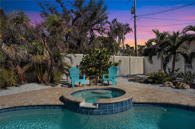 pool at dusk with an in ground hot tub