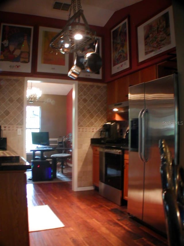 kitchen featuring hardwood / wood-style floors, hanging light fixtures, a chandelier, ventilation hood, and appliances with stainless steel finishes