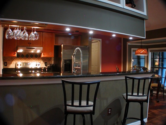 bar with backsplash, dark hardwood / wood-style floors, pendant lighting, and appliances with stainless steel finishes