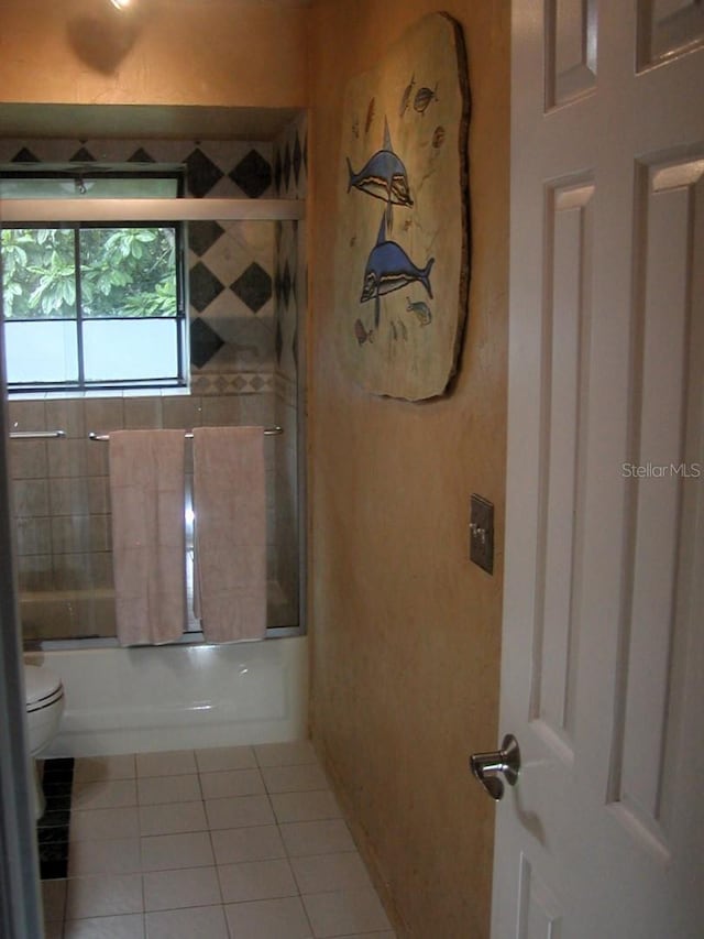 bathroom featuring toilet, combined bath / shower with glass door, and tile patterned flooring