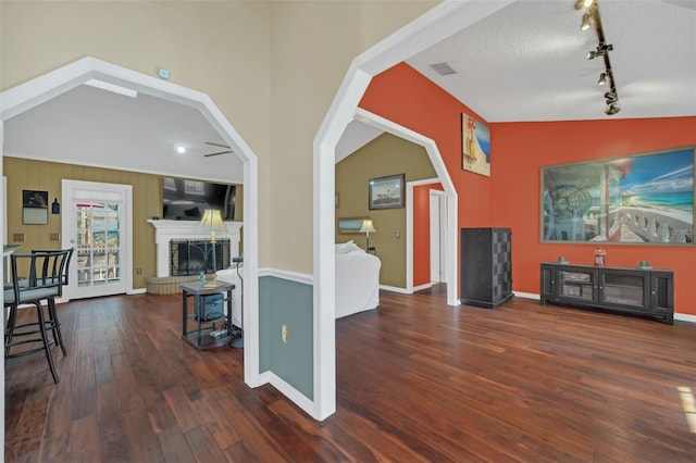 living room with lofted ceiling, dark wood-type flooring, rail lighting, a fireplace, and a textured ceiling