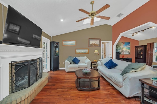 living room featuring rail lighting, vaulted ceiling, a brick fireplace, dark hardwood / wood-style flooring, and ceiling fan