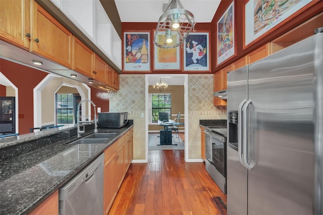 kitchen featuring sink, hanging light fixtures, dark stone countertops, hardwood / wood-style flooring, and stainless steel appliances