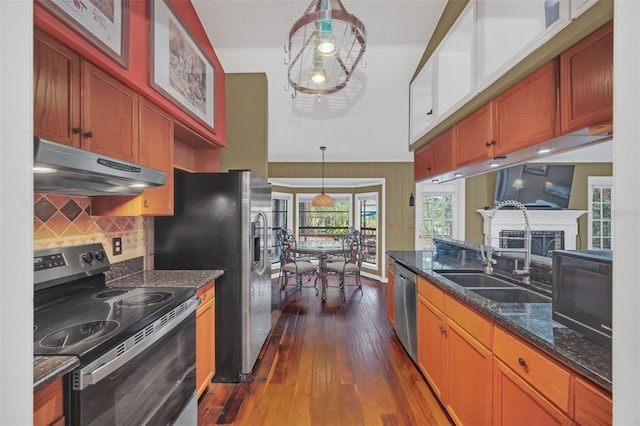 kitchen featuring appliances with stainless steel finishes, decorative light fixtures, sink, dark stone countertops, and dark hardwood / wood-style flooring